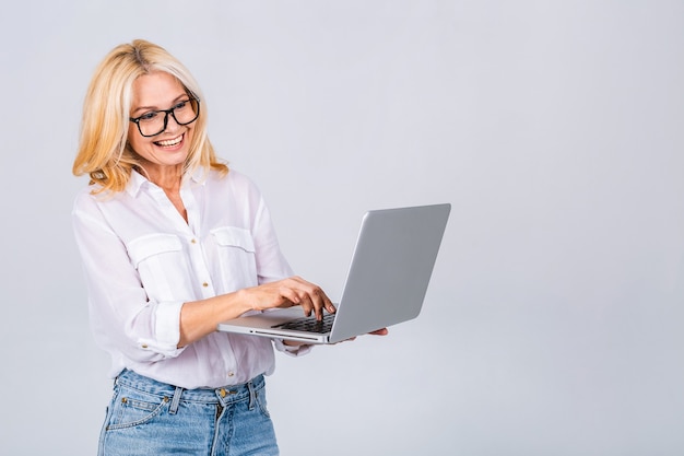 Image of cheerful mature business woman standing isolated over white background using laptop computer. Portrait of a smiling senior lady holding laptop computer.