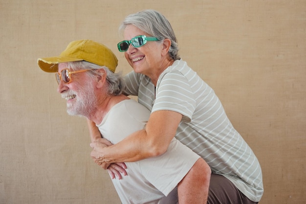 Photo image of cheerful senior couple with colored sunglasses having fun while man piggyback his wife isolated over clear background