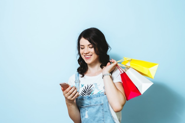 Image of a cheerful young woman showing blank screen mobile phone while carrying isolated over yellow wall shopping bags