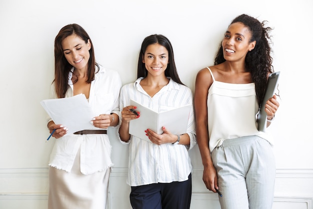 Image of cheery happy young business women colleagues isolated over white wall holding documents work.