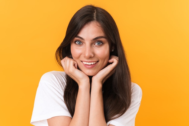 Image closeup of adorable brunette woman with long hair smiling and touching her cheeks isolated over yellow wall