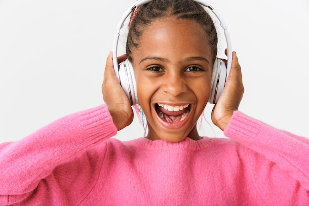 Image closeup of amazed african american girl using headphones while singing isolated over white wall