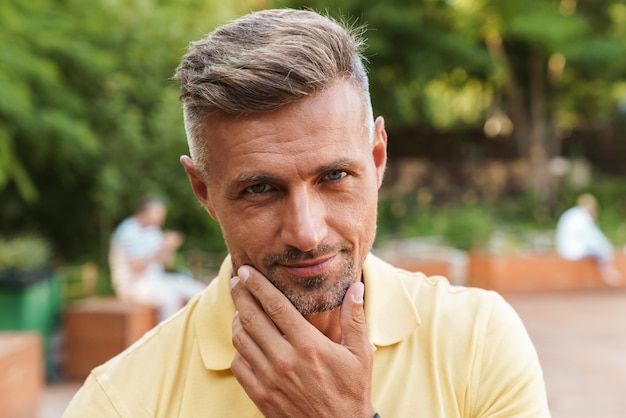 Image closeup of handsome middle-aged man touching his chin while walking in summer park