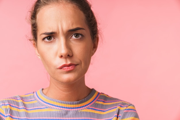 Image closeup of puzzled beautiful woman dressed in colorful clothes frowning and looking isolated over pink wall