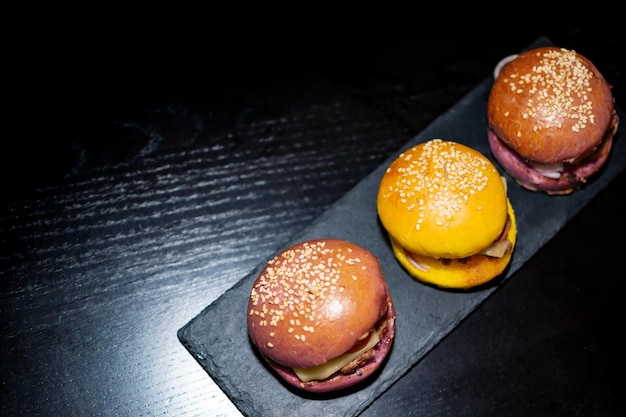 Foto immagine di mini hamburger gourmet colorati con semi di sesamo su tavola di ardesia nera