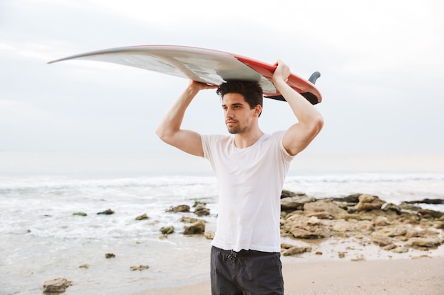 Image of a concentrated handsome man surfer with surfing on a beach outside.