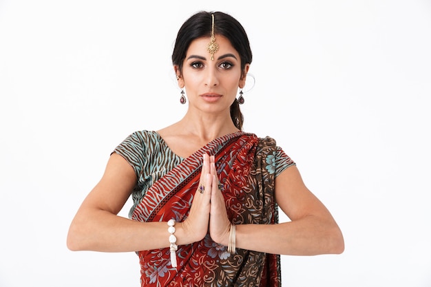 Image of concentrated hindus girl wearing traditional indian costume or saree dress praying with palms together isolated