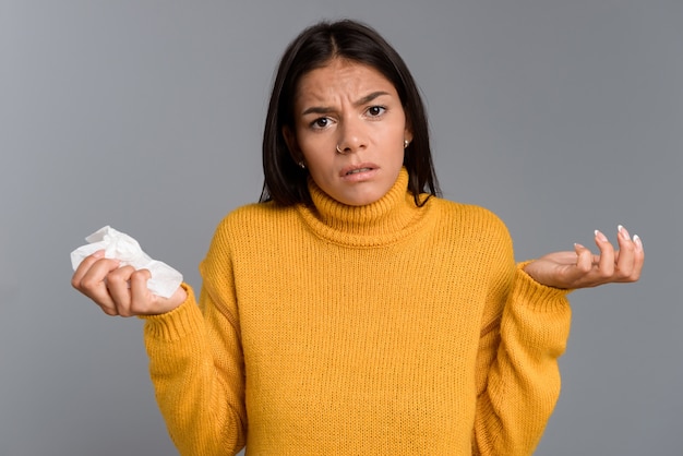 Image of confused ill woman standing isolated over grey wall wall holding napkin.