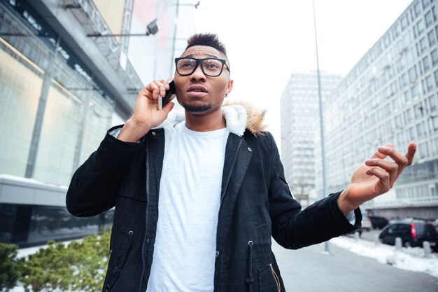 Image of a confused young man walking on the street while talking by his cellphone.