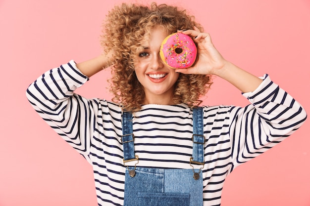 立ったままドーナツを食べるカジュアルな服を着た20代の巻き毛の女性コンテンツの画像