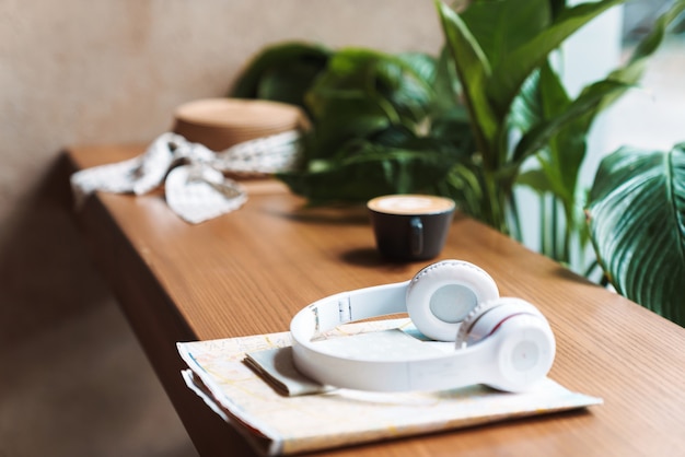 Image of cup of coffee, headphones, passport, paper map lying on wooden table in cafe indoors