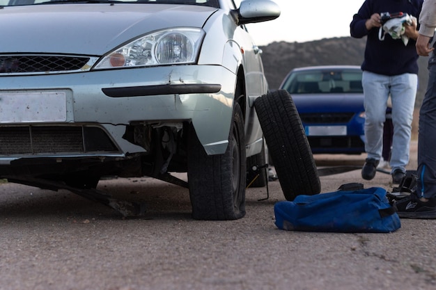 Photo image of a damaged car after an accident and some unrecognizable people about to change a flat tire