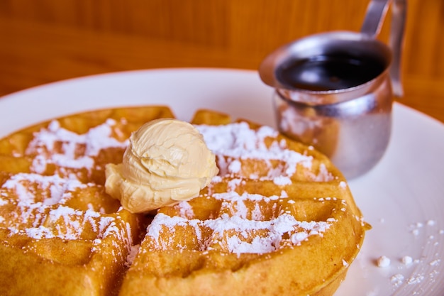 Image of Delicious and sweet simple waffle with powdered sugar, butter dollop, and silver container of syrup