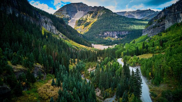 Foto immagine di una strada sterrata in fondo a una valle aperta circondata da montagne e ricoperta di foreste di pini