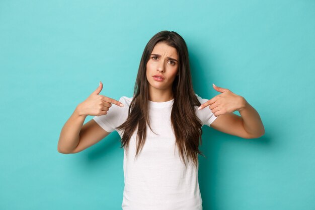 Image of disappointed pretty girl in white t-shirt, complaining and pointing at center logo, showing