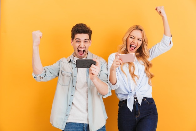 Image of ecstatic man and woman rejoicing while playing together video games on mobile phones