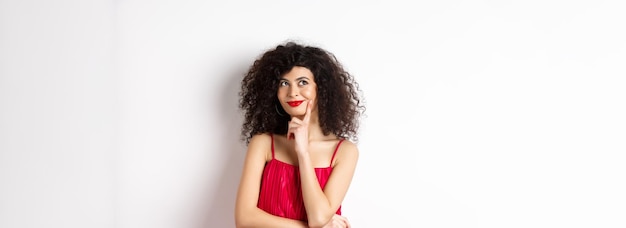 Image of elegant woman in red dress looking pensive and smiling thinking of romantic date standing o