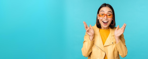 Immagine di una giovane donna asiatica entusiasta che celebra trionfante guardando sorpreso e felice applaudendo le mani soddisfatte in piedi su sfondo blu