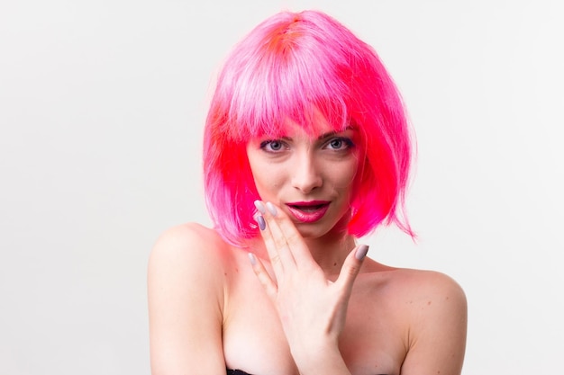 Image of excited beautiful woman in wig laughing while posing with candy isolated over pink background