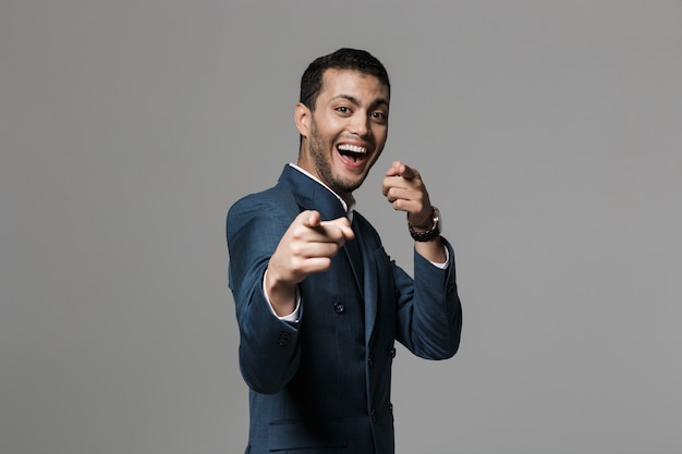 Image of excited happy business man isolated over grey wall wall pointing.