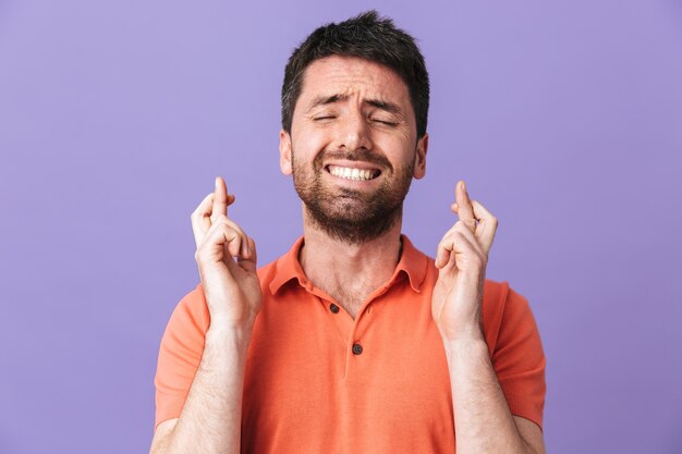 L'immagine di un giovane uomo barbuto bello e nervoso eccitato che posa isolato su un muro viola viola fa un gesto speranzoso per favore.