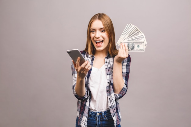 Image of excited young lady. Amazed with mobile phone, holding money.