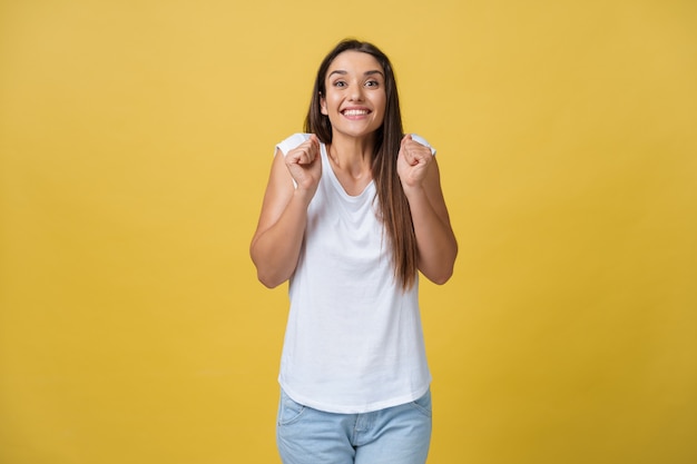 黄色の背景の上に孤立して立っている興奮した若い女性の画像。探しているカメラ。