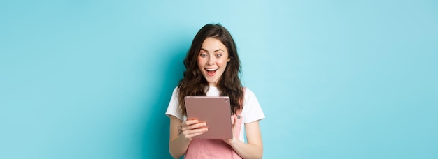 デジタル タブレットの画面に驚いて興奮した若い女性の凝視のイメージは、何かクールなオンライン st を見つけた