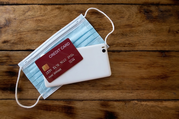 An image of a face mask, mobile phone and credit card blank on a wooden table. Top View.