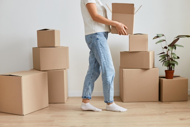 Image of faceless anonymous unknown woman wearing jeans and white shirt holding cardboard box in hands unpacking parcels during relocating to another flat