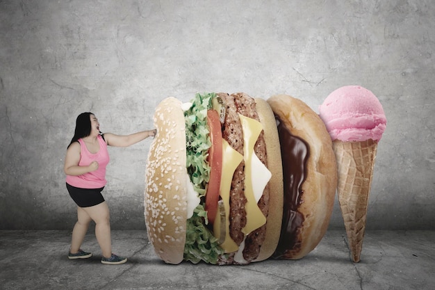 image of fat woman wearing sportswear while fighting with junk foods. diet concept