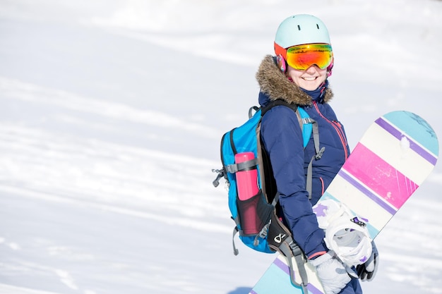 Image of female athlete wearing helmet with backpack and snowboard