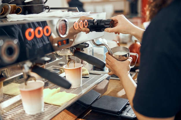 コーヒーメーカーを使用してカフェでミルクを蒸す女性バリスタの画像。