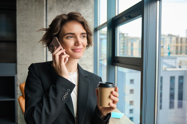 オフィスに立って窓の外を眺めながら電話に応答する女性起業家の画像