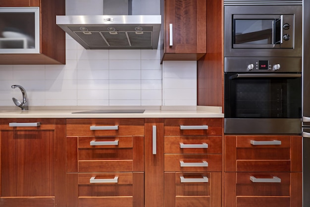 Image of the front of a kitchen with reddish wood cabinets with many metal handles and integrated stainless steel appliances