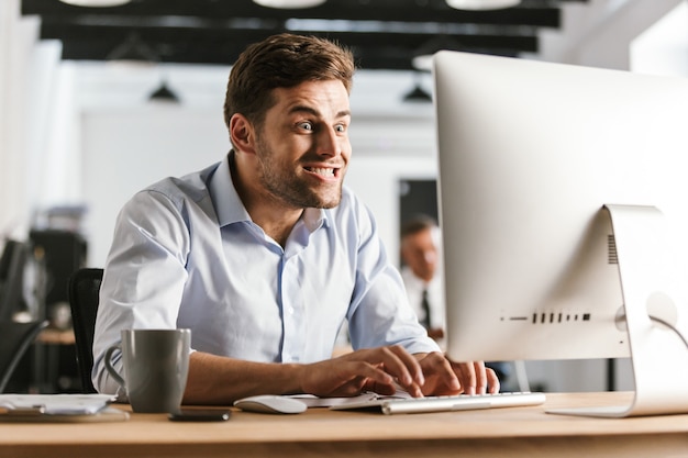 Photo image of funny business man using computer while sitting by the table in office