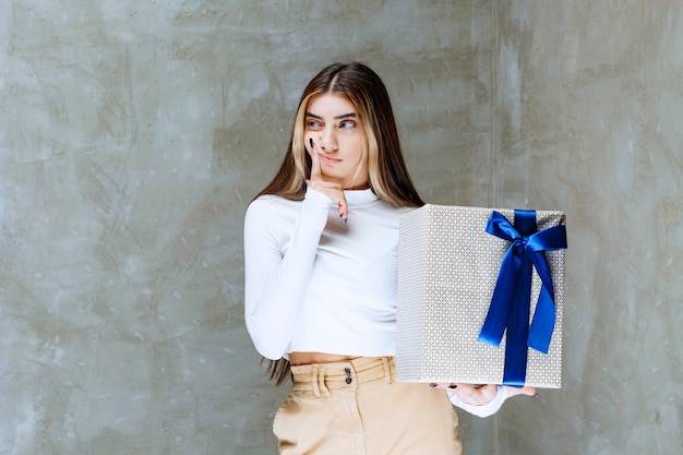 Image of a girl model holding a present box with bow isolated over stone