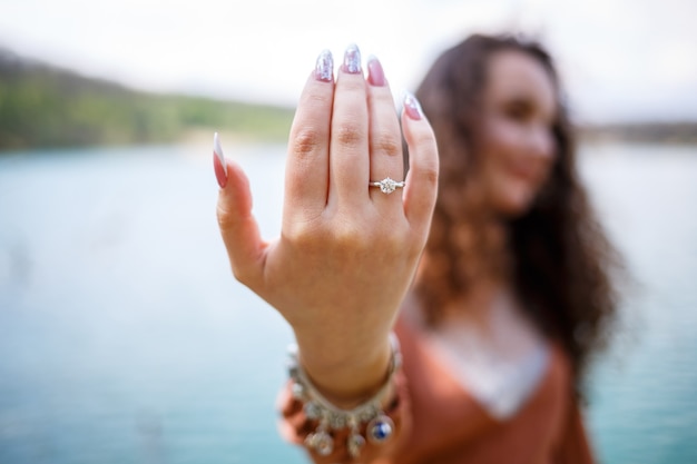 屋外で、女性の手に銀の結婚指輪を付けた女の子の画像。海や川の背景