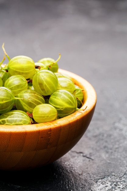 Image of gooseberry berries in wooden cup on black background