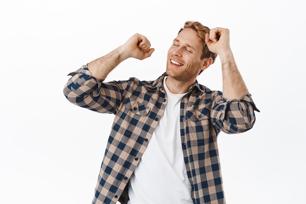 Image of handsome adult redhead man dancing with closed eyes, happy face and smile, relaxing on dance floor, enjoying music, standing against white background