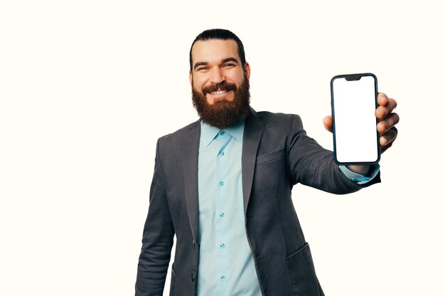 Image of handsome bearded man in suit showing you smartphone blank white screen isolated on white