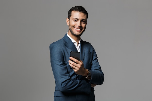 Image of handsome business man holding mobile phone posing isolated over grey wall wall.