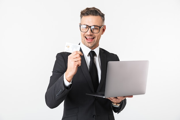 신용 카드를 들고 노트북 컴퓨터를 사용 하여 흰 벽 위에 절연 잘 생긴 비즈니스 남자의 이미지.