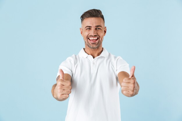 Image of a handsome excited emotional adult man posing over blue wall showing thumbs up.