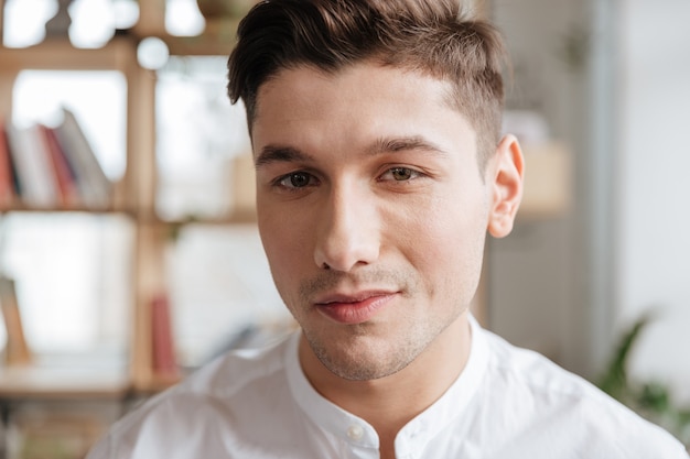 Image of handsome man dressed in white shirt standing indoors. Coworking. Looking at camera.