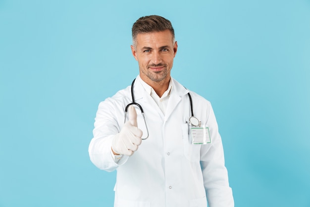 Image of a handsome mature man doctor posing isolated over blue wall wall showing thumbs up.