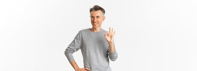 Photo image of handsome middleaged man in grey sweater showing okay sign and smiling satisfied recommend p