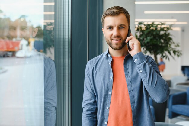 Image of handsome serious young man talking cellphone while working at office