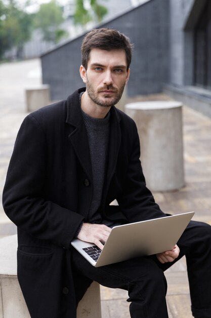 Image of handsome young businessman sitting outdoors using laptop computer.