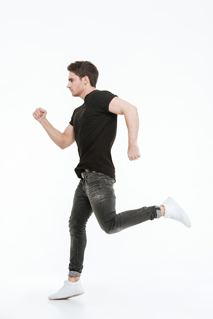 Image of handsome young man dressed in black t-shirt running over white background looking aside.